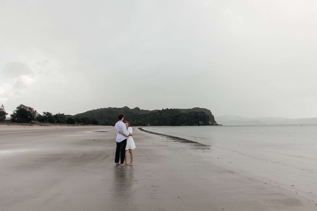 Romantic couple portrait by Cooks Beach photographer with waves and coastal scenery in the background