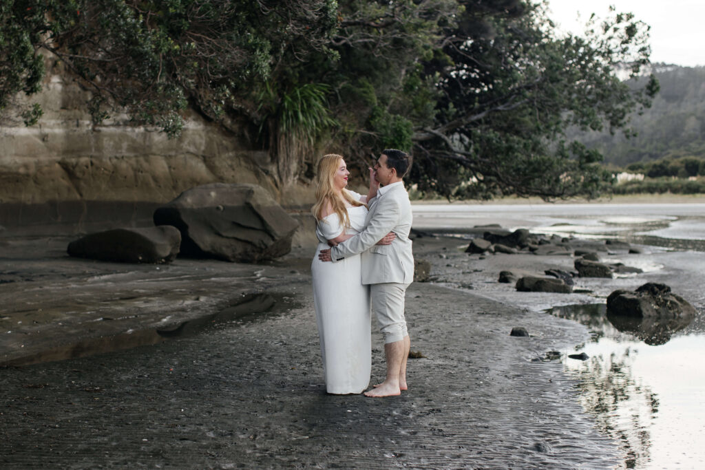 Couple walking with husky dog along sandy flats at Kakamatua Inlet, West Auckland photo location for candid engagement photos.