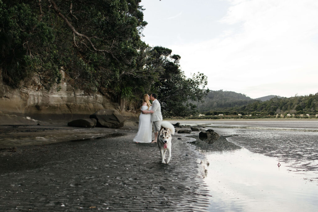 Romantic couple holding hands on rocky shoreline at Kakamatua Inlet, West Auckland engagement photography.