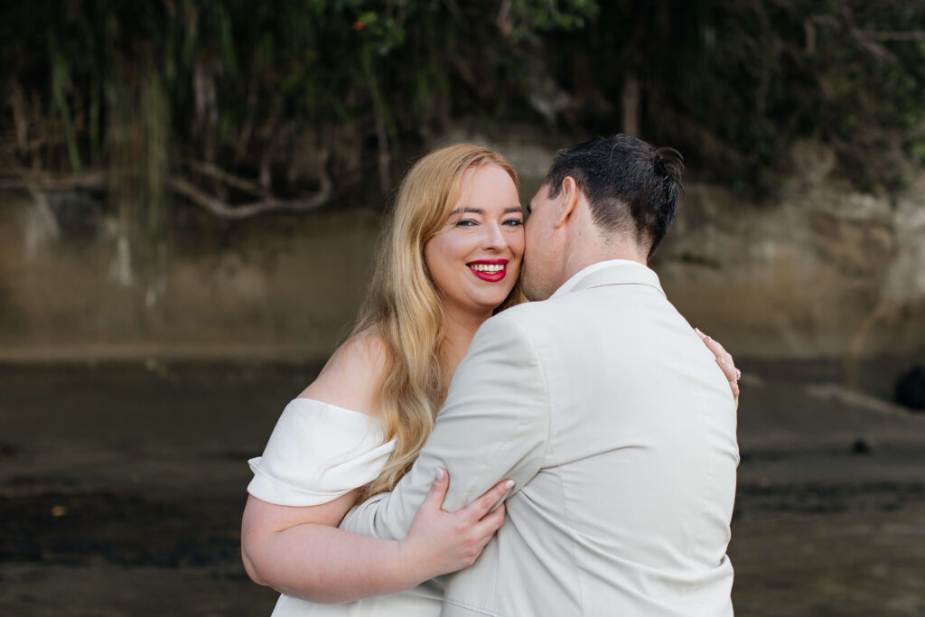 Candid moment of couple laughing together after slipping on rocks during West Auckland engagement session.