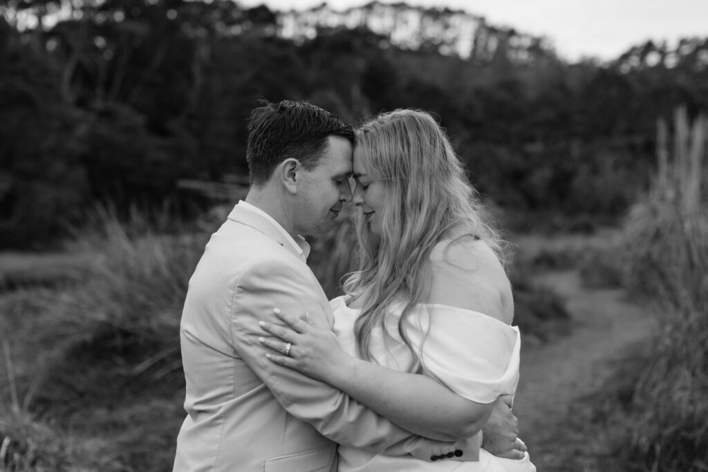 Romantic couple holding hands on rocky shoreline at Kakamatua Inlet, West Auckland engagement photography.