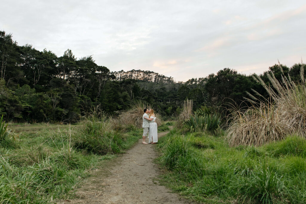Romantic couple holding hands on rocky shoreline at Kakamatua Inlet, West Auckland engagement photography.
