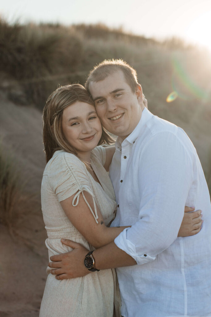 Engaged couple embracing in front of dunes at Hot Water Beach Coromandel