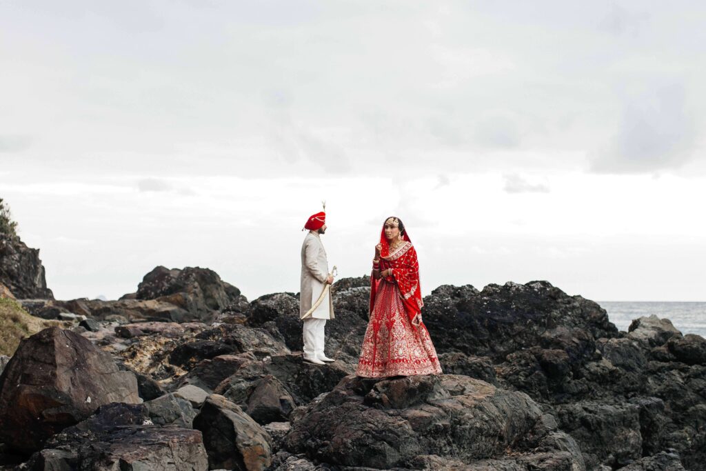 Bride and Groom in their traditional Indian wedding outfits on the beach rocks.