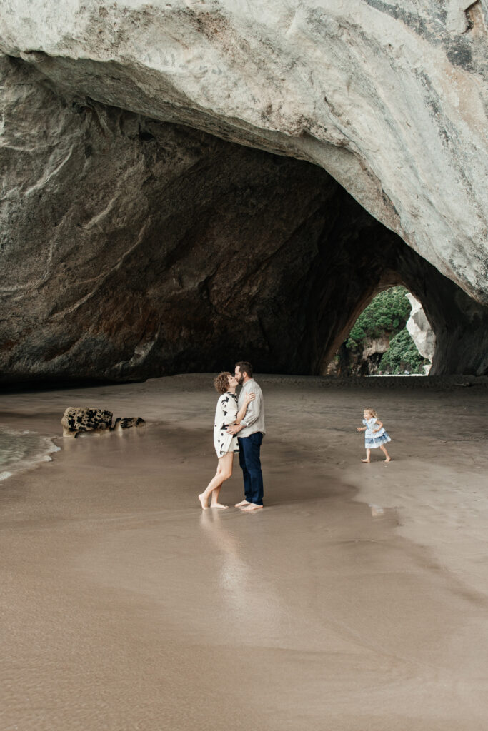 Parents holding hands with child in front of the famous Cathedral Cove rock arch – Cathedral Cove family photos