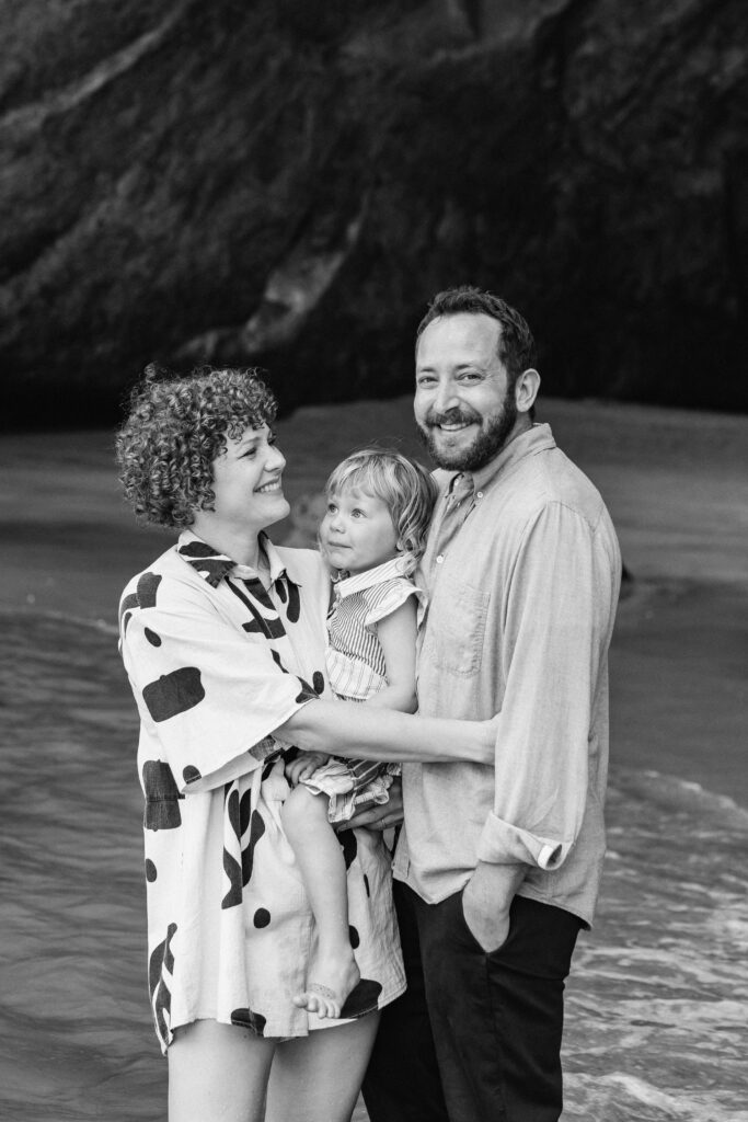 Parents holding hands with child in front of the famous Cathedral Cove rock arch – Cathedral Cove family photos