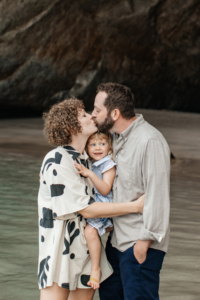 Parents holding hands with child in front of the famous Cathedral Cove rock arch – Cathedral Cove family photos