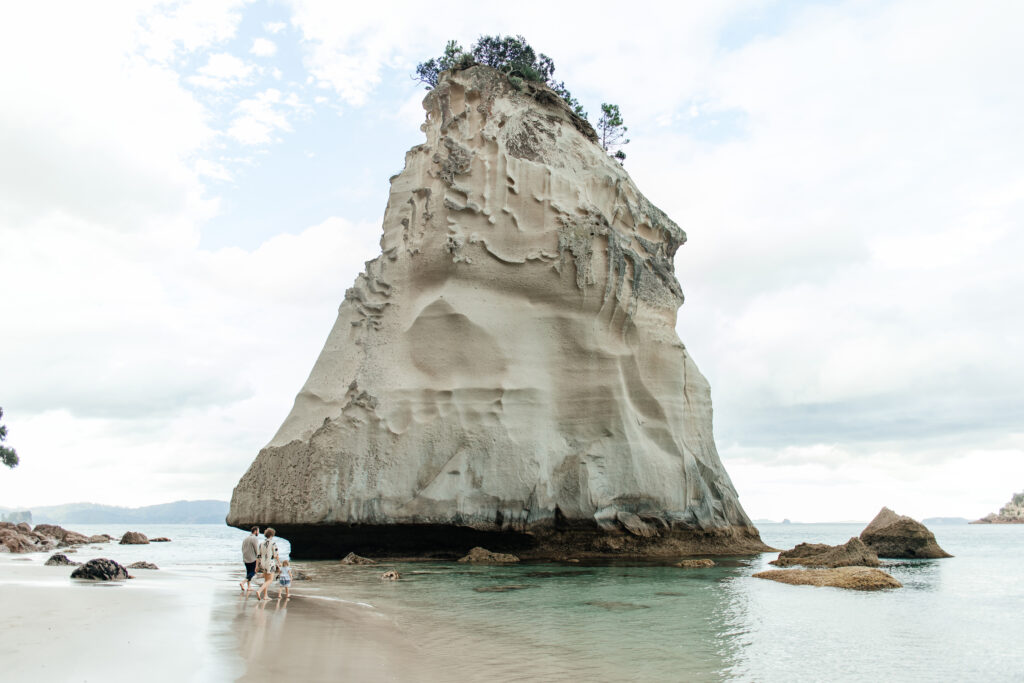 Portrait of parents at Cathedral Cove with ocean cliffs in background – family photography Coromandel