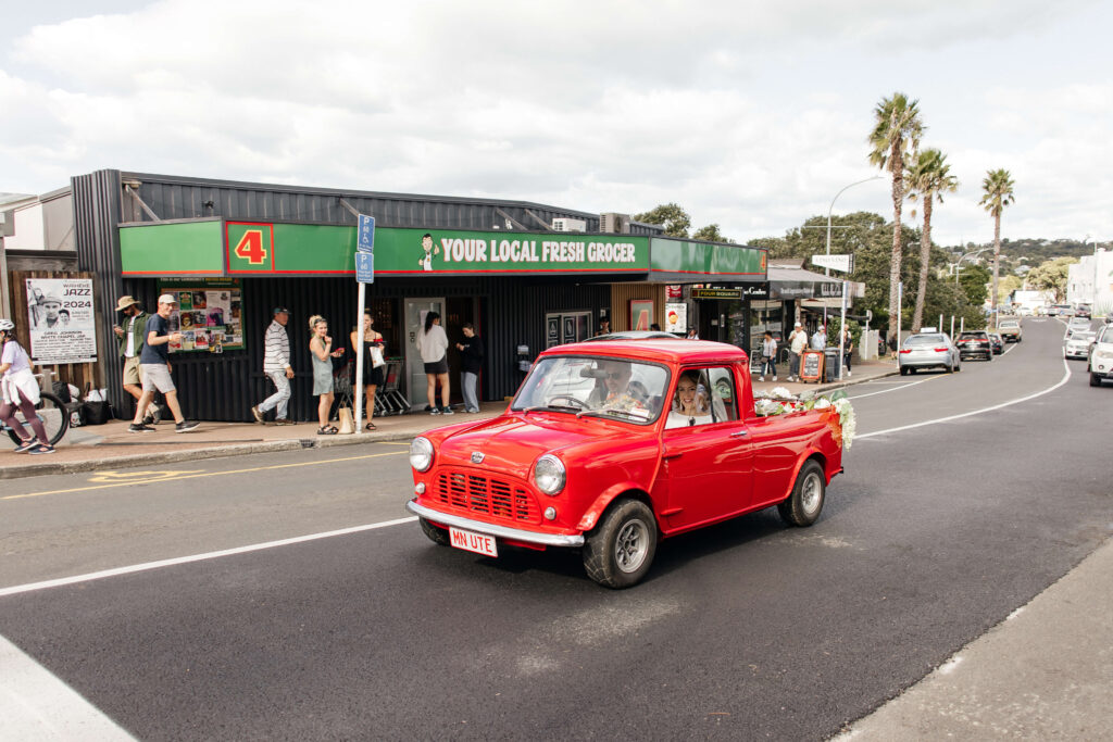 Bride driving through Oneroa in a vintage Mini before their wedding at Mudbrick – Waiheke Island wedding photography