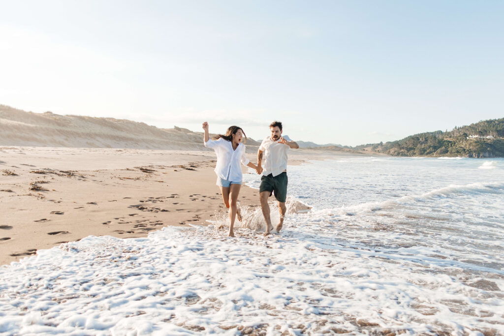 Candid moment of couple embracing at sunset with waves in the background – Coromandel engagement photographer