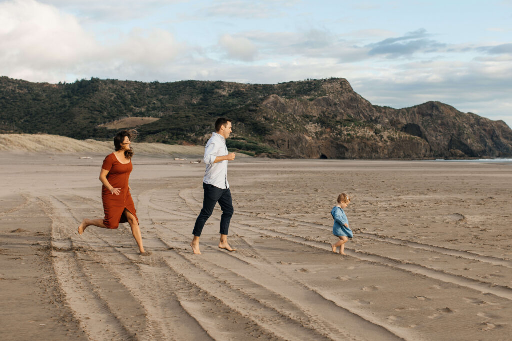 Family of three walking along Bethells Beach at sunset
