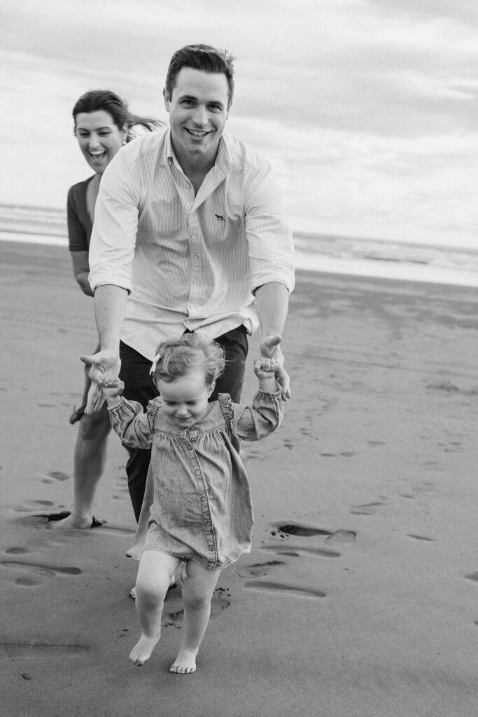 Family of three walking along Bethells Beach at sunset