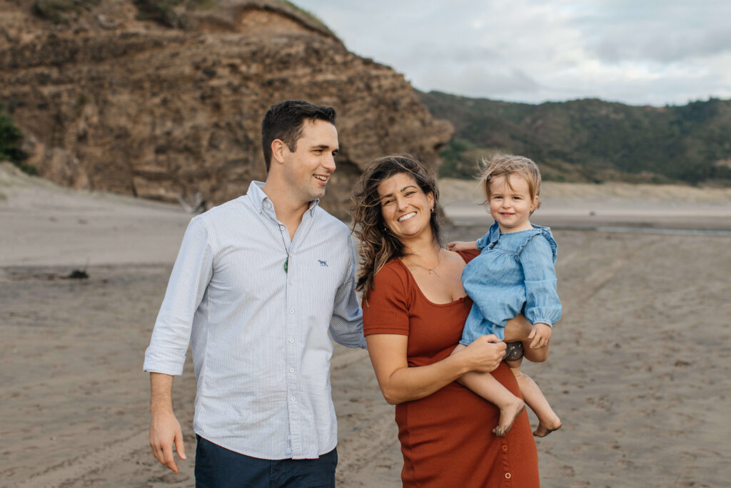 Parents holding daughter on windy Bethells Beach evening