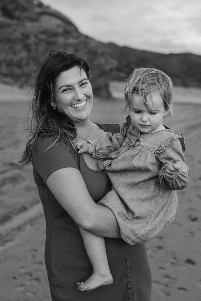 Mum hugging daughter during golden hour at Bethells Beach