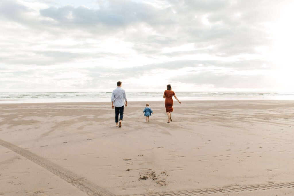 Family of three walking along Bethells Beach at sunset