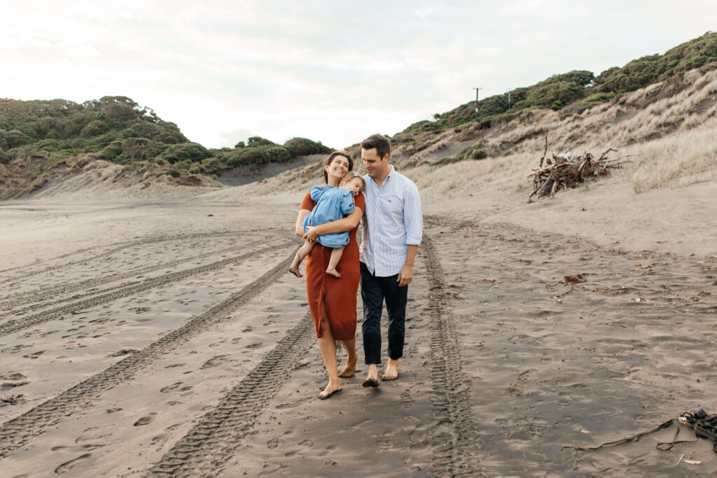 Parents holding daughter on windy Bethells Beach evening