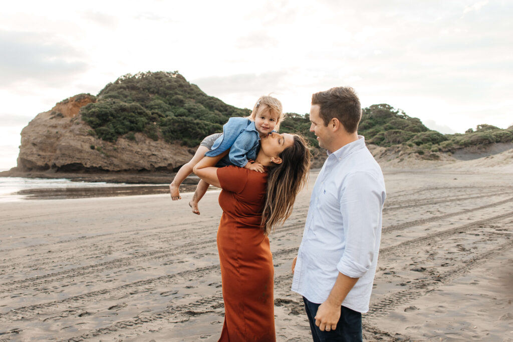 Parents holding daughter on windy Bethells Beach evening