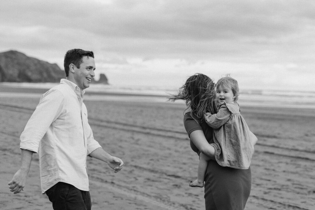 Parents holding daughter on windy Bethells Beach evening