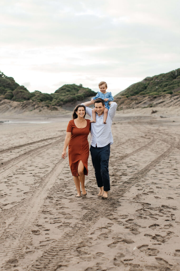 Parents holding daughter on windy Bethells Beach evening