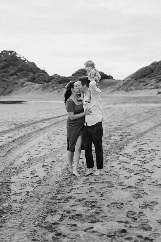 Parents holding daughter on windy Bethells Beach evening
