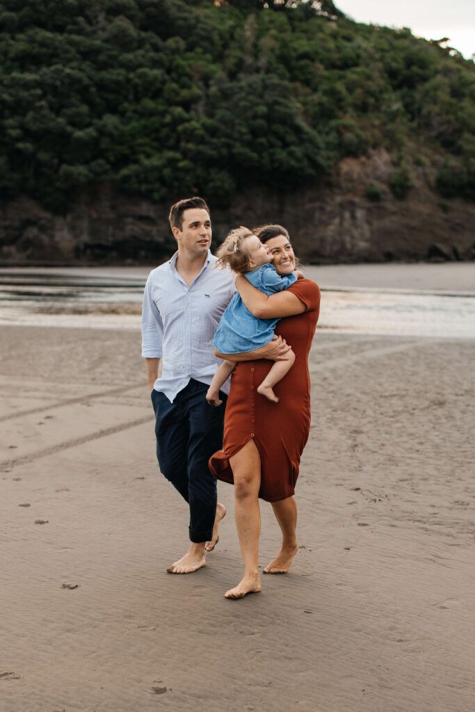 Parents holding daughter on windy Bethells Beach evening