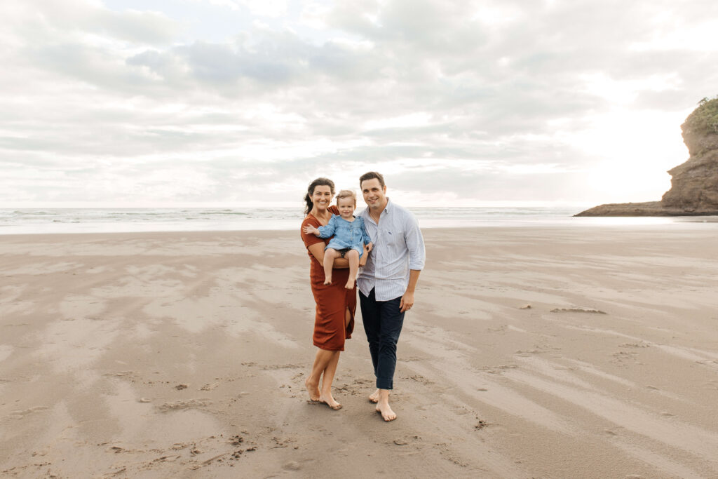 Parents holding daughter on windy Bethells Beach evening