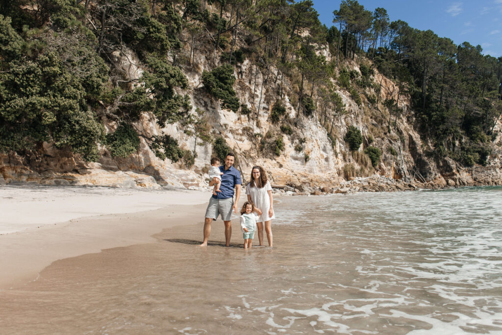 Family of four walking along Hahei Beach during sunny morning photo session in New Zealand