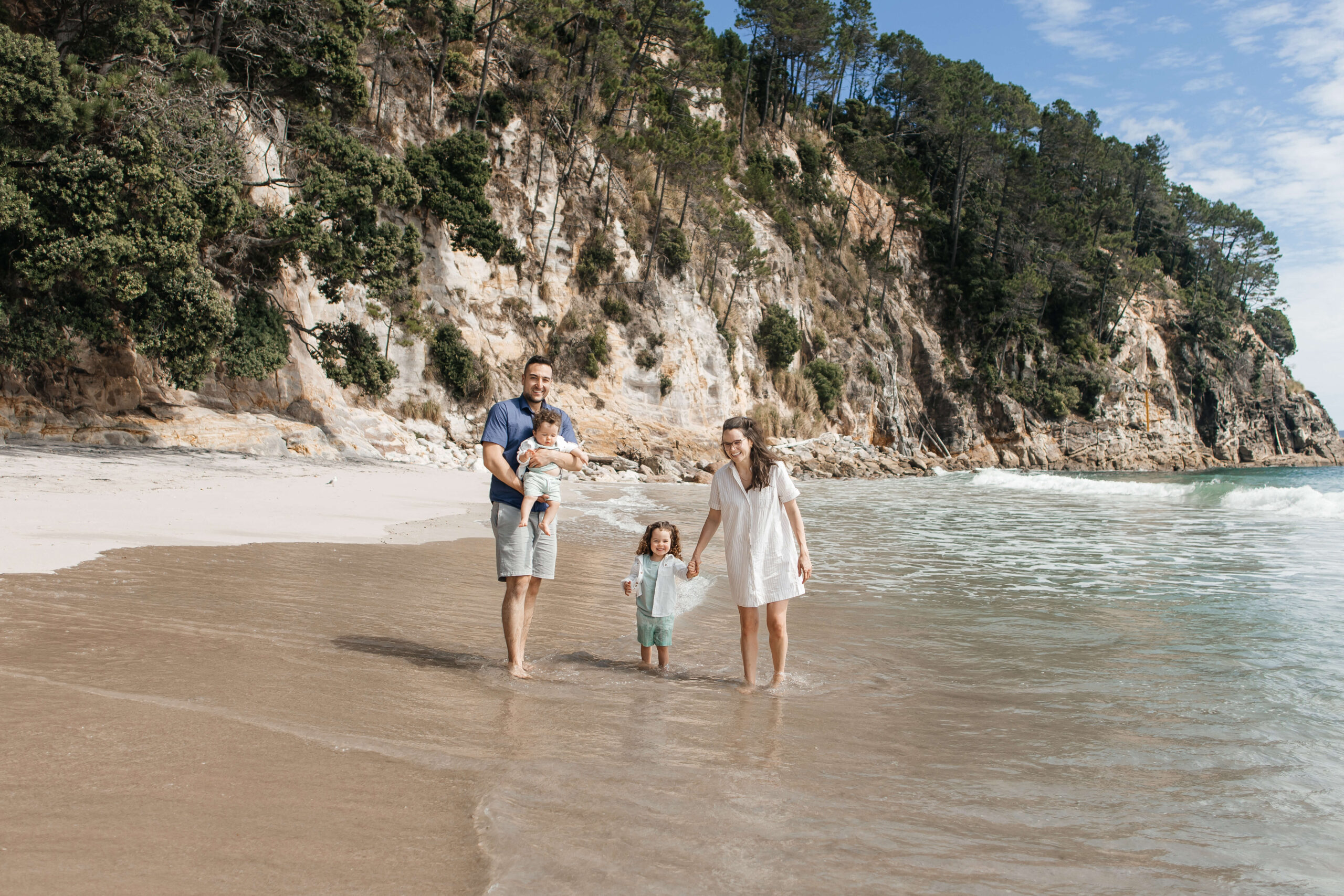 Family of four walking along Hahei Beach during sunny morning photo session in New Zealand