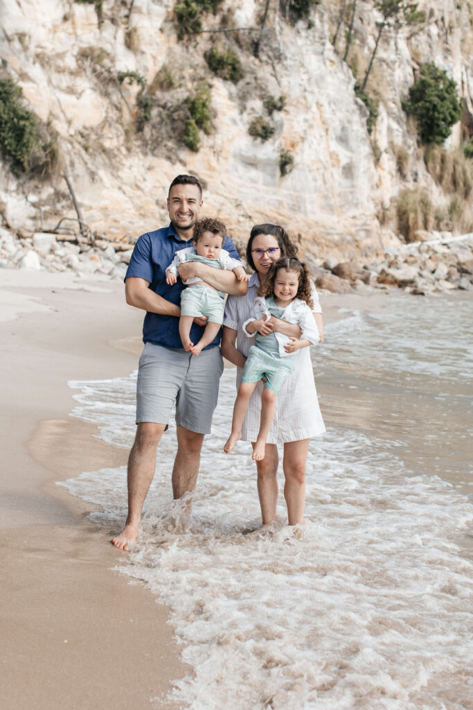 Family of four walking along Hahei Beach during sunny morning photo session in New Zealand
