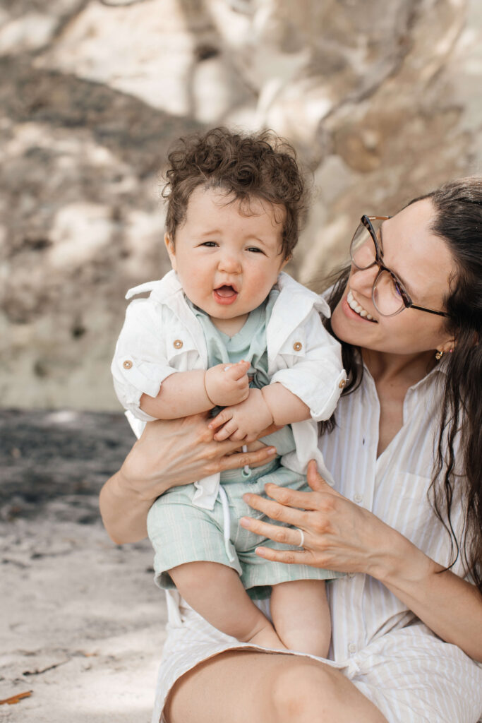 Baby boy smiling while being held by his mum during Hahei Beach family photos