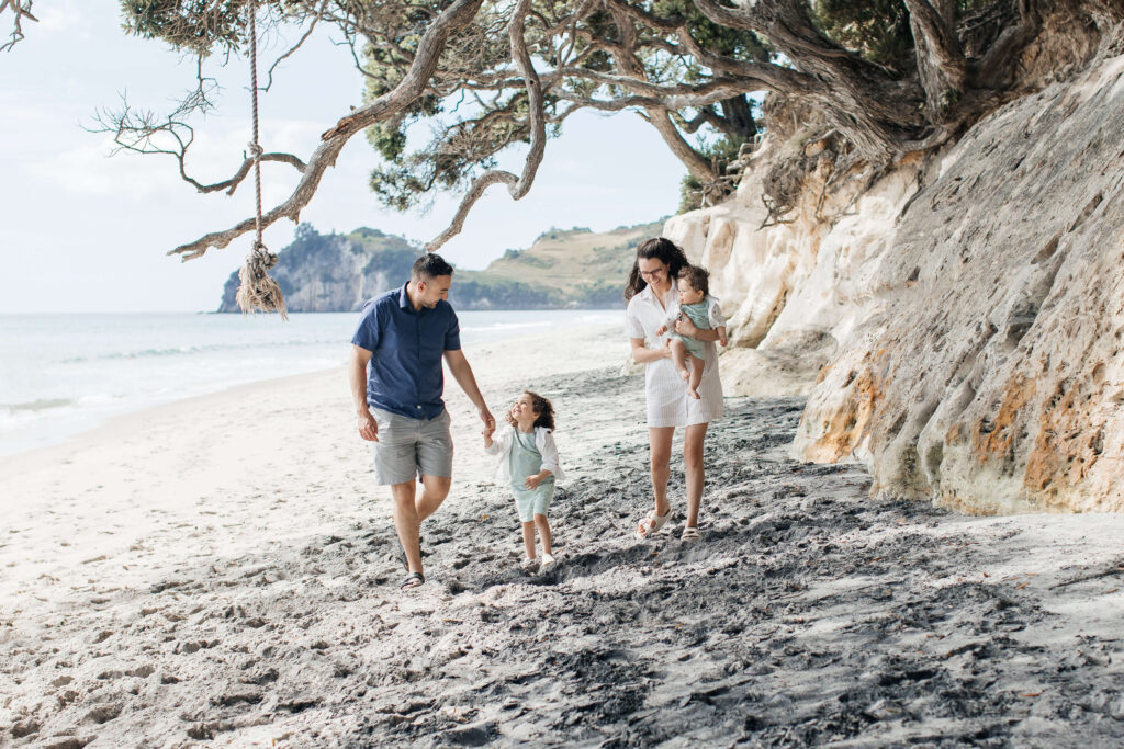 Family of four walking along Hahei Beach during sunny morning photo session in New Zealand