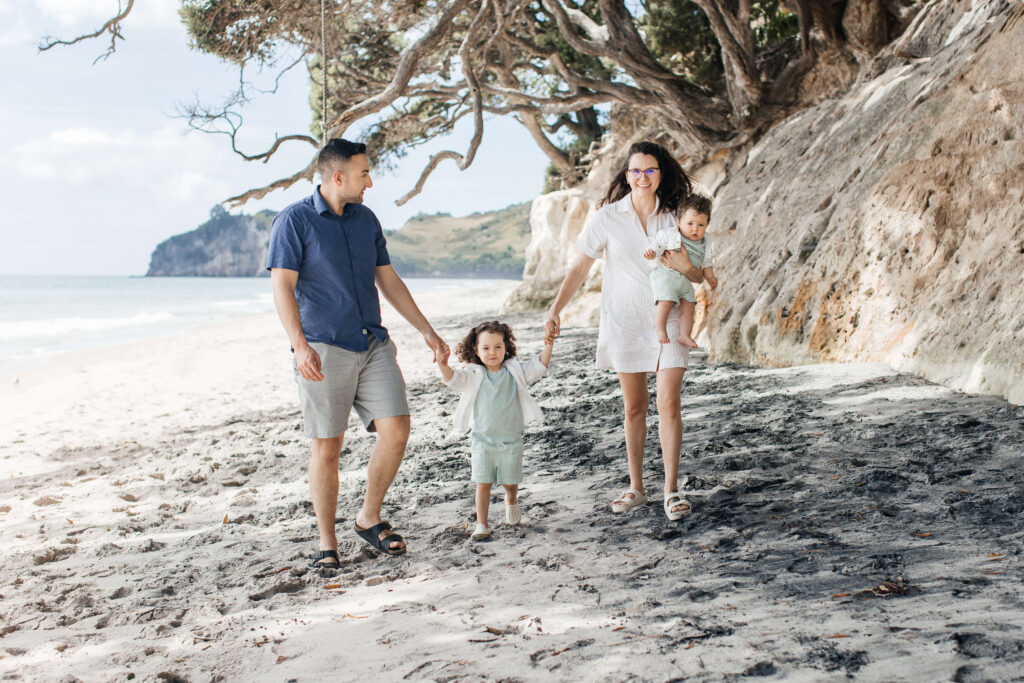 Family of four walking along Hahei Beach during sunny morning photo session in New Zealand