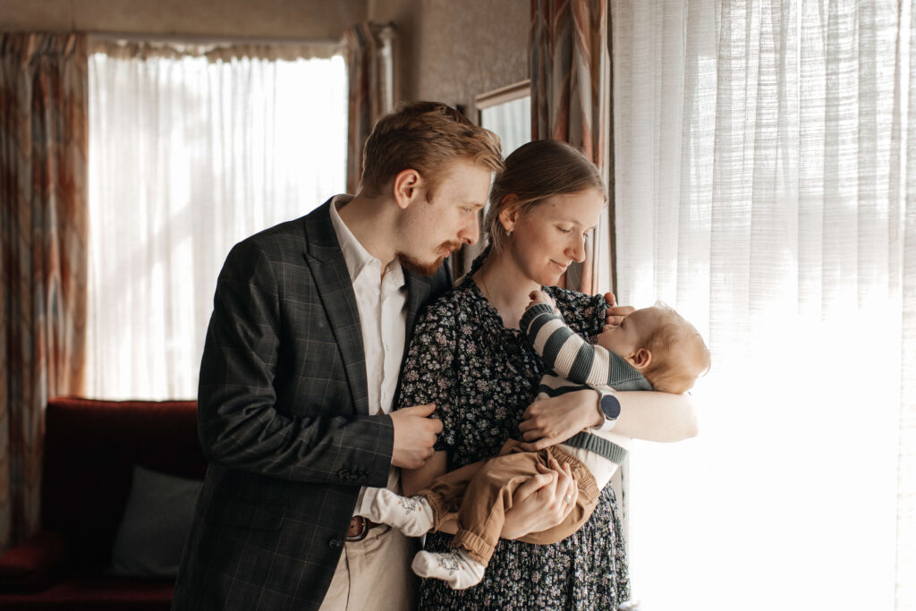 Mother cuddling her young son by the window, captured in soft natural light during their family photo session at home.