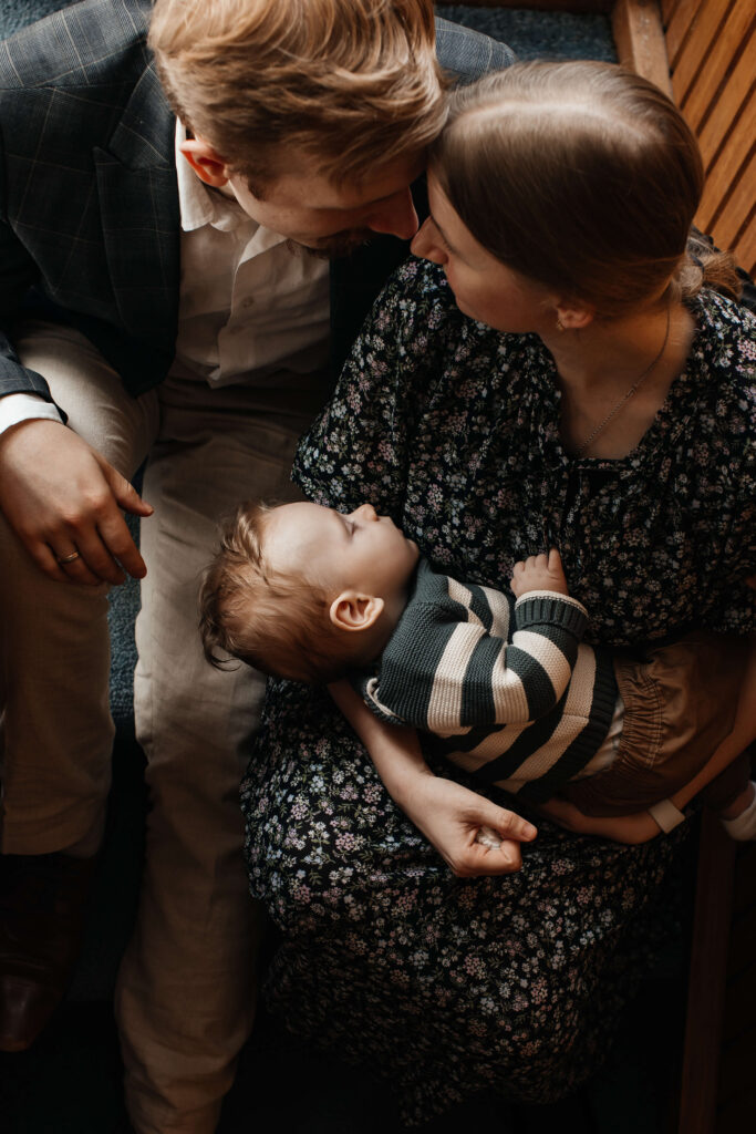Parents laughing while playing with their young son in the living room during an at-home lifestyle family photoshoot.