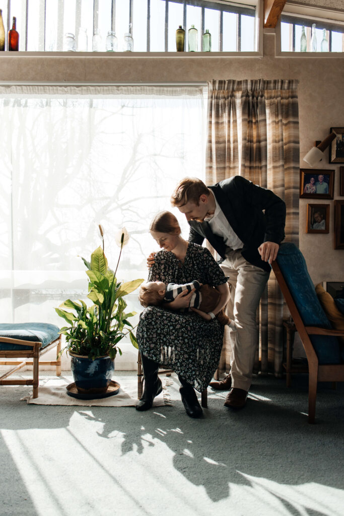 Parents laughing while playing with their young son in the living room during an at-home lifestyle family photoshoot.