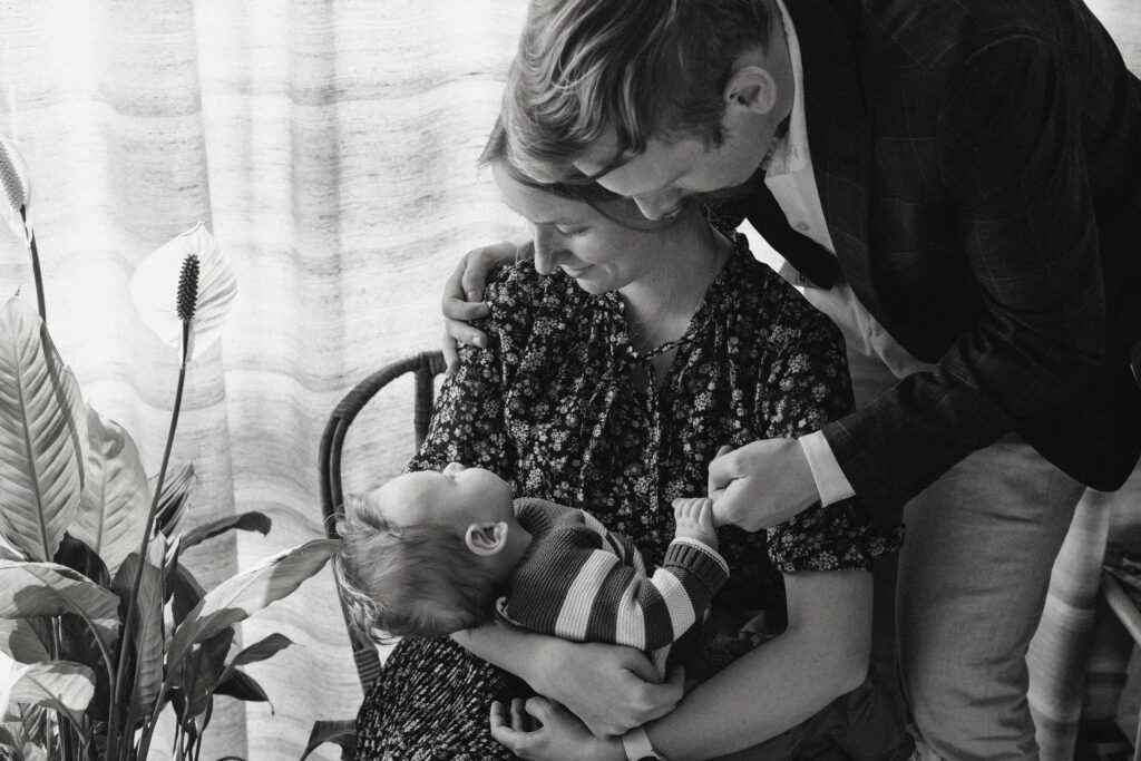 Parents laughing while playing with their young son in the living room during an at-home lifestyle family photoshoot.