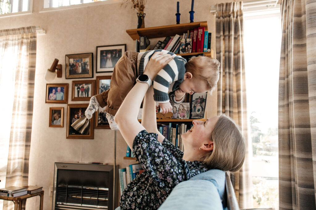 Parents laughing while playing with their young son in the living room during an at-home lifestyle family photoshoot.