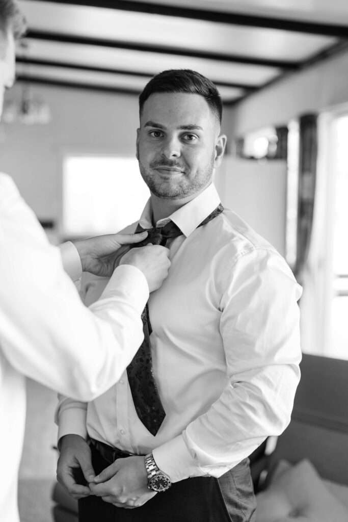 Groom preparing for Old Forest School wedding day in Pukehina with estuary views.